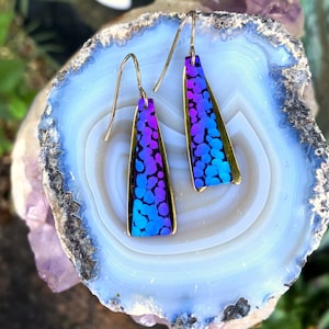 May include: A pair of dangle earrings with a gold frame and a blue and purple iridescent enamel design. The enamel has a speckled pattern.