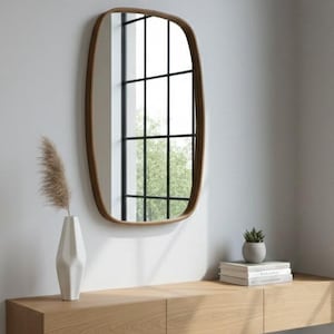 Peut inclure: Intérieur moderne avec une étagère flottante en bois, un miroir décoratif et un vase blanc avec des herbes de la pampa séchées. Une petite plante en pot et des livres sont sur l'étagère. Le miroir a un cadre marron.