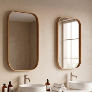 May include: A modern bathroom vanity with two round, white sinks and matching wooden-framed mirrors. The vanity has a light wood finish with two drawers. Accessories include soap dispensers, a brush, and rolled white towels.