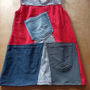 Peut inclure: Une robe en patchwork rouge, bleu et gris avec un motif de peau de serpent blanc. La robe est sans manches et comporte plusieurs poches.