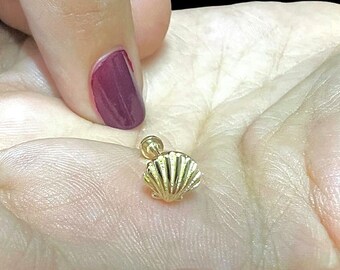 May include: A gold seashell body jewelry piercing. The seashell is detailed and has a textured surface.