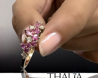 May include: A gold ring with a cluster of pink and white gemstones. The ring is set with a variety of sizes and shapes of stones, creating a unique and eye-catching design.