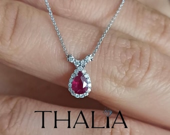 Op de afbeelding: Een delicate zilveren ketting met een peervormige robijn hanger omringd door een halo van kleinere diamanten. De hanger hangt aan een delicaat Y-vormig ontwerp.