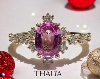 May include: A pink oval gemstone ring with a halo of small diamonds set in yellow gold. The ring has a delicate band with additional diamonds.