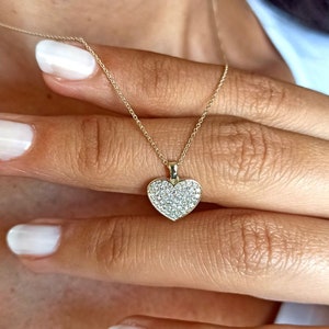 Puede incluir: Un collar de cadena de oro con un colgante en forma de corazón cubierto de pequeños diamantes.