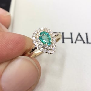 Puede incluir: Un anillo de esmeralda en forma de pera con un halo doble de diamantes engastado en oro amarillo.