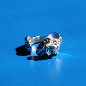 Peut inclure: Une bague en argent avec un design texturé et organique. Une pierre précieuse bleue est sertie au centre de la bague.
