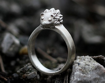 May include: A silver ring with a hedgehog design. The hedgehog is detailed with small eyes and a textured body.