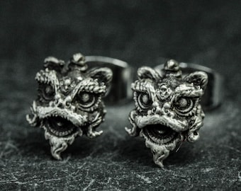 May include: A pair of silver lion dance head cufflinks. The cufflinks are detailed with intricate carvings and have a realistic appearance.