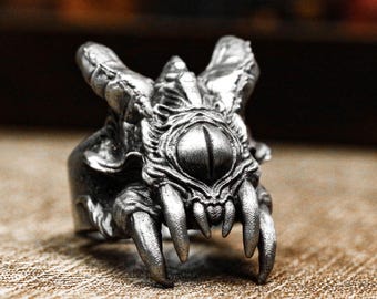 May include: A silver ring with a detailed design of a creature with a single large eye and sharp teeth.