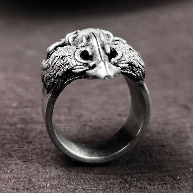May include: A silver ring with a detailed design of a bird's head with wings on either side.
