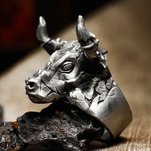 May include: A silver ring with a detailed bull head design. The bull's head is textured and has a realistic appearance.