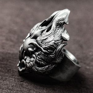 May include: A silver ring with a detailed wolf head design. The wolf's head is facing to the left and has a textured, almost furry appearance. The ring is made of metal and has a smooth, polished finish.