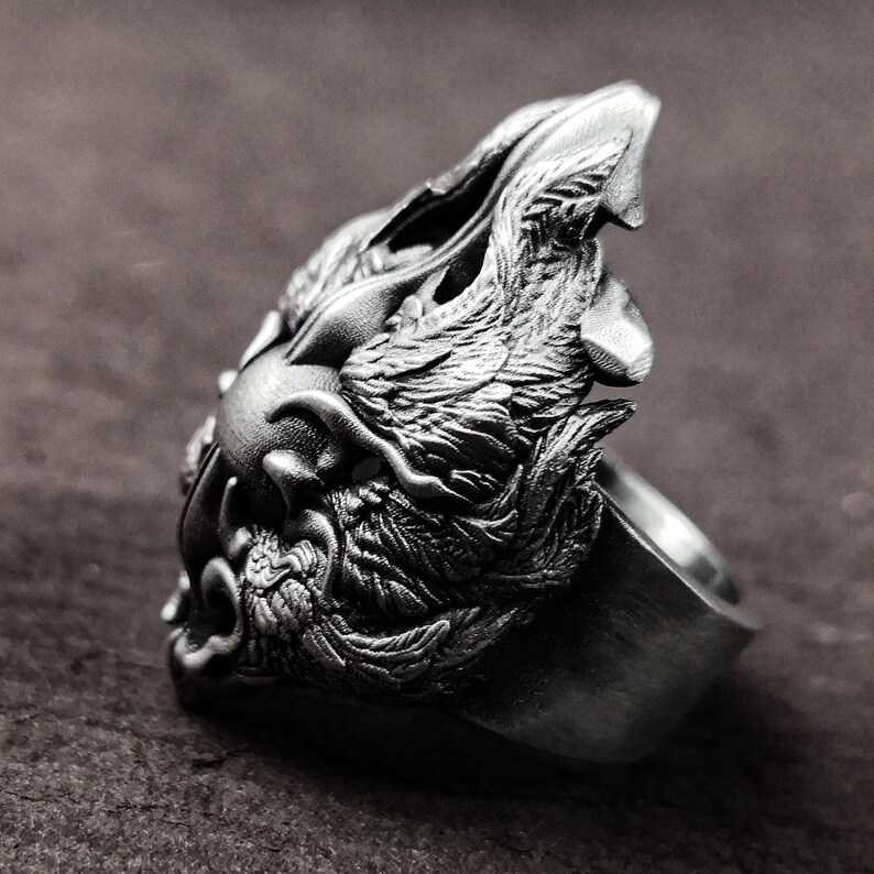 May include: A silver ring with a detailed wolf head design. The wolf's head is facing to the left and has a textured, almost furry appearance. The ring is made of metal and has a smooth, polished finish.