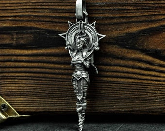 May include: A silver pendant featuring a detailed depiction of a woman with a headdress and a long, flowing gown. The pendant is surrounded by a circular design with a starburst pattern.