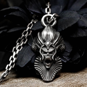 Peut inclure: Un collier avec un pendentif en argent représentant un crâne détaillé avec une couronne et un col à volants. Le pendentif est attaché à une chaîne en argent.