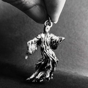 May include: A silver-colored pendant shaped like a ghost, with a flowing, draped robe. The pendant is hanging from a silver chain.