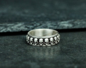 May include: A silver ring with a band of small skull details.