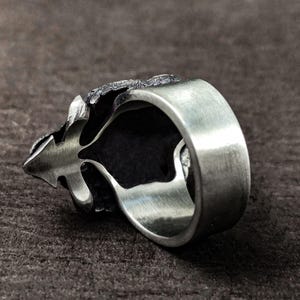 May include: A silver ring with a detailed, textured design. The ring is open on one side and has a smooth, polished band.