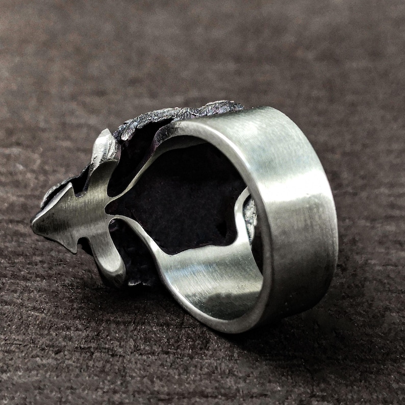 May include: A silver ring with a detailed, textured design. The ring is open on one side and has a smooth, polished band.