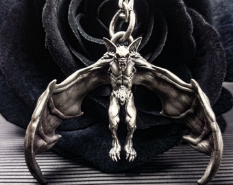 May include: A silver bat pendant with outstretched wings, hanging from a silver chain. The pendant is detailed with a snarling bat face and a muscular body.