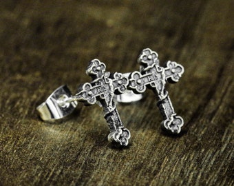 May include: A pair of silver cross earrings with intricate details. The crosses are slightly raised and have a textured surface.