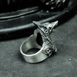 K&ouml;nnte beinhalten: Ein silberner Ring mit detailliertem Wolfskopf-Design. Der Ring hat eine offene R&uuml;ckseite und ein Ankh-Symbol an der Seite. Das Metall hat eine geb&uuml;rstete Oberfl&auml;che, die ihm ein Vintage-Aussehen verleiht. Ein auff&auml;lliges Schmuckst&uuml;ck.