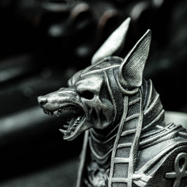 K&ouml;nnte beinhalten: Eine detaillierte, silberfarbene Skulptur von Anubis, dem alt&auml;gyptischen Gott der Unterwelt. Die Skulptur zeigt Anubis mit dem Kopf eines Schakals, offenem Mund und aufgerichteten Ohren. Die Figur ist mit traditionellen &auml;gyptischen Details verziert.