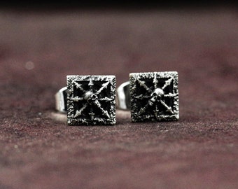 May include: A pair of silver stud earrings with a square design featuring a skull in the center. The skull is surrounded by a detailed, intricate pattern.