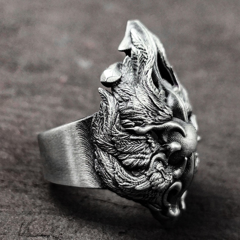 May include: A silver ring with a detailed, textured design of a wolf's head. The ring is made of metal and has a smooth band.