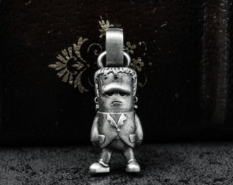 May include: A silver charm pendant featuring a cartoon-style Frankenstein's monster wearing a suit. The charm has a detailed design and a slightly sad expression.