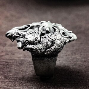 May include: A silver ring with a detailed design of two wolves intertwined. The ring is made of metal and has a smooth finish.