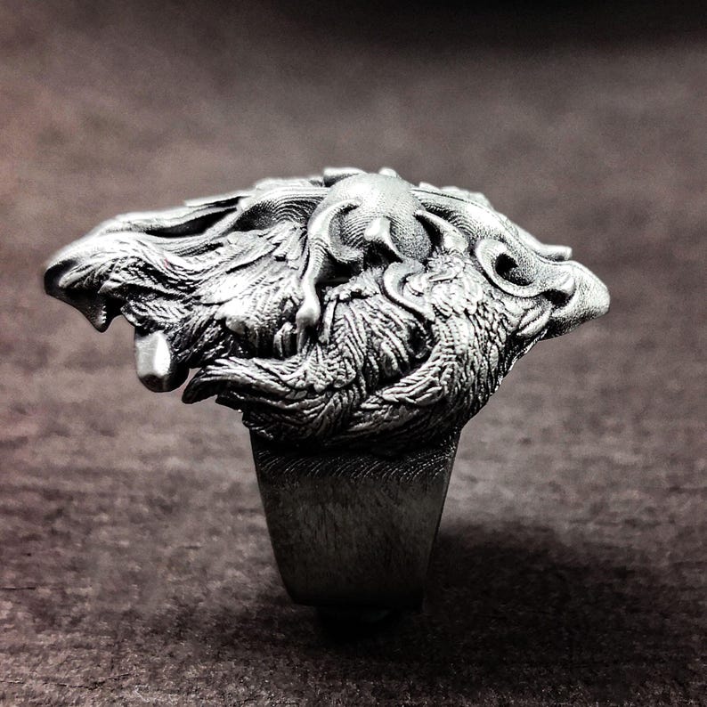 May include: A silver ring with a detailed design of two wolves intertwined. The ring is made of metal and has a smooth finish.