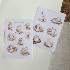 Könnte beinhalten: Zwei Blätter mit Aufklebern, die verschiedene Kaffeegetränke mit Schlagsahne und herbstlichen Designs zeigen. Der Text "Sticker Sheet" erscheint auf jedem Blatt.