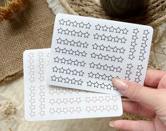 May include: Two sheets of white sticker paper with rows of black and brown outline star stickers.