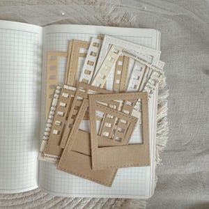 Könnte beinhalten: Ein Satz brauner und weißer Papiersticker für Fotorahmen mit genähten Kanten. Die Sticker sind auf einer Notizbuchseite mit einem Rastermuster angeordnet. Der Text "Liebestöter wurden" ist auf der Seite sichtbar.