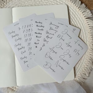 Könnte beinhalten: Ein Satz transparenter Aufkleberbögen mit handgeschriebenen Zahlen, Wochentagen und Monaten. Die Aufkleber sind perfekt für Planer, Journale und andere Papierarbeiten.