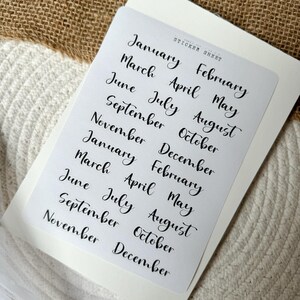 Könnte beinhalten: Eine Sticker-Tabelle mit den Monaten des Jahres in Schreibschrift. Die Tabelle enthält zwei Sätze aller zwölf Monate, von Januar bis Dezember.