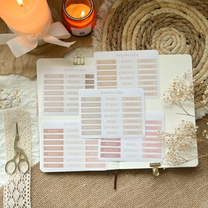 Könnte beinhalten: Ein Satz von sieben wöchentlichen Planer-Aufklebern mit den Wochentagen in einer minimalistischen Schrift. Die Aufkleber sind in Beige- und Rosatönen.
