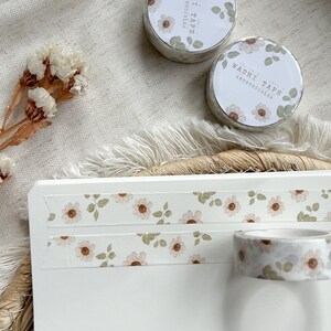 Könnte beinhalten: Zwei Rollen florales Washi-Tape mit dem Text "WASHI TAPE ARTSTUDIO.LA" auf einer Rolle. Das Band befindet sich auf einer weißen Oberfläche mit einem floralen Design.