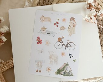 Pode incluir: Uma folha de adesivos com tema cottagecore que inclui um coelho branco, uma bicicleta, uma cabana, uma borboleta, flores e uma cesta de morangos. A folha de adesivos diz "Sticker Sheet" no topo.