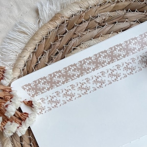 Könnte beinhalten: Zwei Streifen braunes, gemustertes Washi-Tape auf weißem Hintergrund. Das Muster ist ein sich wiederholendes Blumenmuster.