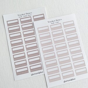May include: Two sheets of stickers with a gradient design. The stickers are rectangular with rounded corners and have a white border. The text "Tracker Boxes" is printed on each sheet, along with the color of the stickers. The first sheet has the text "Small - Antique Mauve" and the second sheet has the text "Small - Taupe".