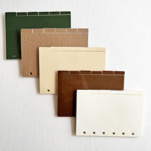 May include: A set of five rectangular planner dividers in varying shades of dark green, tan, cream, brown, and off-white. Each divider features a top tab and a series of circular punched holes along the left side for insertion into a binder system.