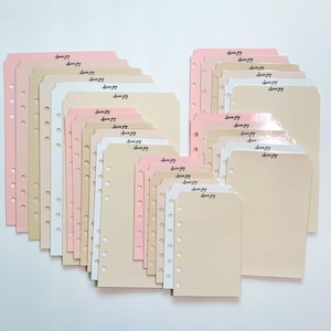 May include: A collection of planner dividers in various shades of pink, beige, and white. Each divider has a curved top and is pre-punched with holes for binding. The text "Ladybug" is written on each divider in a cursive font.