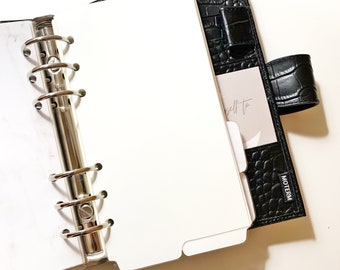 May include: A black leather planner with a silver ring binder and a white page insert. The planner has a crocodile embossed pattern and the text "MOTERM" is printed on the cover.
