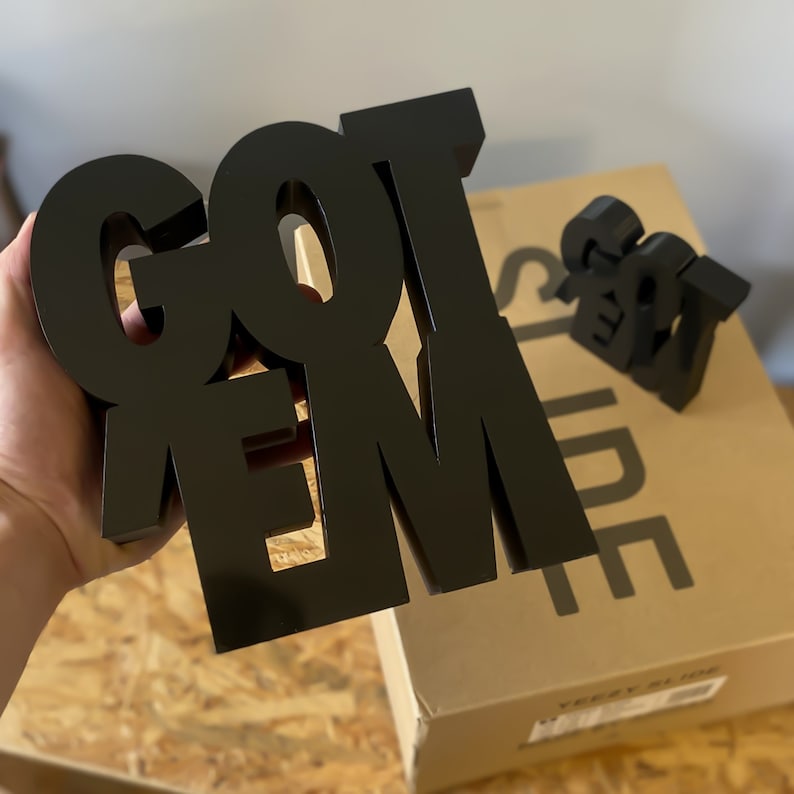 Peut inclure: Lettres en bois noir en bloc orthographiant "GOT EM" sur une bo&icirc;te brune avec le texte "YEEZY SLIDE" imprim&eacute; dessus.