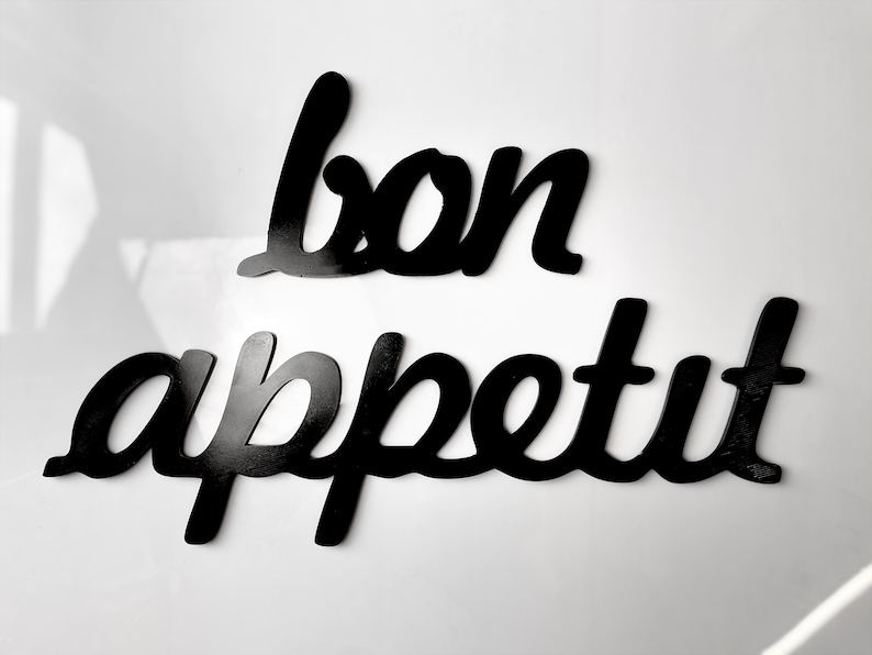 May include: Black wooden letters spelling out "bon appetit" on a white background.