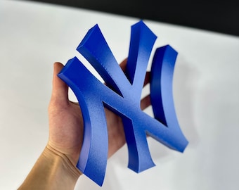 以下が含まれることがあります： 青い3Dプリントされたニューヨーク・ヤンキースのロゴ。ロゴは、曲線的なデザインのスタイリッシュな「NY」です。