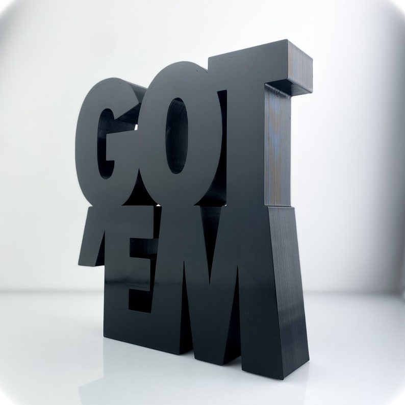 Peut inclure: Sculpture en 3D noire et autonome des mots &laquo; GOT 'EM &raquo; en lettres majuscules. La sculpture est faite d'un mat&eacute;riau noir lisse.